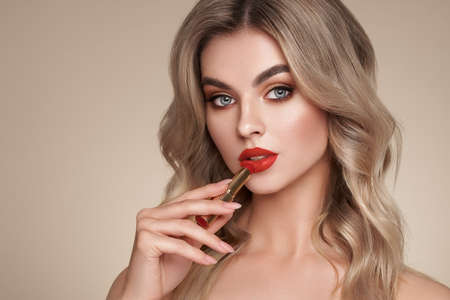A beautiful young blonde woman applying lipstick. Model with healthy skin, close up portrait. Cosmetology, beauty and spaの写真素材