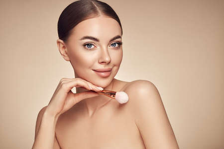 Portrait beautiful young woman with clean fresh skin. Model with cosmetic makeup brush. Cosmetology, beauty and spaの写真素材