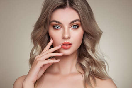 A beautiful young woman with shiny wavy blonde hair. Model with healthy skin, close up portrait. Cosmetology, beauty and spaの写真素材