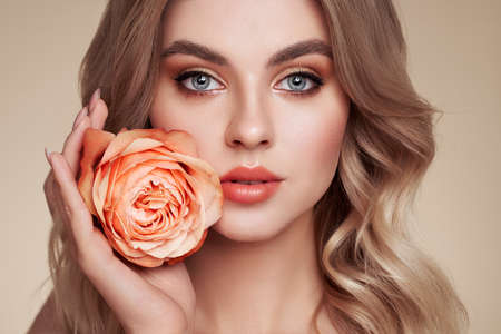 A beautiful young woman with shiny wavy blonde hair. Model with healthy skin, close up portrait. Girl with a rose flowerの写真素材