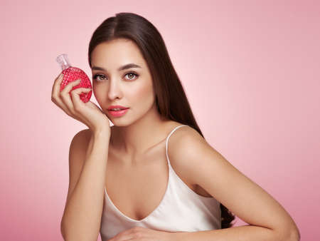 Young beautiful woman with a bottle of perfume. Model with healthy skin, close up portrait. Cosmetology, beauty and spaの写真素材