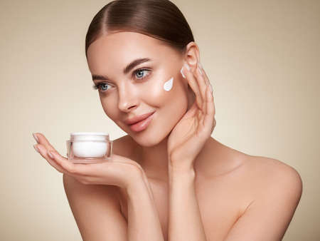Beauty woman applying cream on her face. Young woman with clean fresh skin. Model with a jar of face creamの写真素材