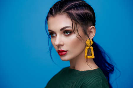 Brunette girl with perfect makeup. Beautiful model woman with curly hairstyle. Care and beauty hair products. Lady with braided hair. Model with jewelry. Blue backgroundの写真素材