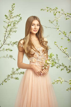Beautiful Woman in Lace Wedding Dress. Beautiful Lady with Healthy and Beauty Hair. The model Poses on the Background of a Blooming Apple Tree. Springtime Photoの写真素材