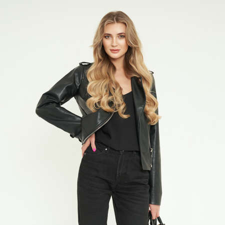 Young blonde woman in black leather jacket and black jeans. Girl posing on a white background. Jewelry and hairstyle. Fashion photoの写真素材