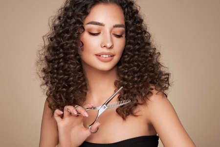 Beautiful young woman with a bright makeup and a afro  hair holds metal scissors. Model with curly hair. Hair salon, haircut. Care and beauty hair products. Perfect make-upの写真素材