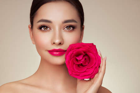 A beautiful young woman with shiny wavy blonde hair. Girl with a rose flower. Model with healthy skin. Cosmetology, beauty and spaの写真素材