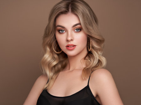 A beautiful young woman with shiny wavy blonde hair. Model with healthy skin, close up portrait. Cosmetology, beauty and spaの写真素材