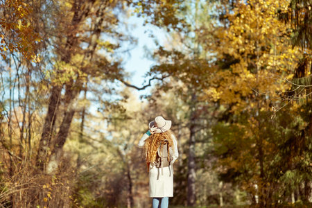 A young red-haired woman walks through the autumn park. A girl in a beige hat looks at the autumn forestの写真素材