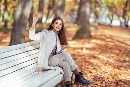 A young beautiful woman is sitting on a bench in an autumn park. A girl listen to music in the autumn forestの写真素材