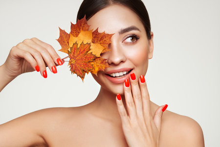 Portrait of beautiful young woman with autumn maple leafs. Healthy clean fresh skin natural make up beauty eyes and red nailsの写真素材