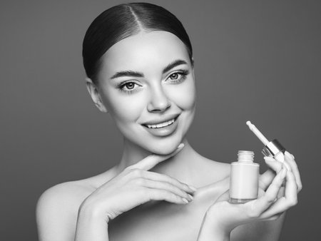 Portrait beautiful young woman with clean fresh skin. Model with foundation makeup bottle. Cosmetology, beauty and spaの写真素材