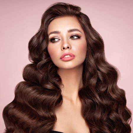 Brunette girl with perfect makeup. Smiling beautiful model woman with long curly hairstyle. Care and beauty hair products.の写真素材