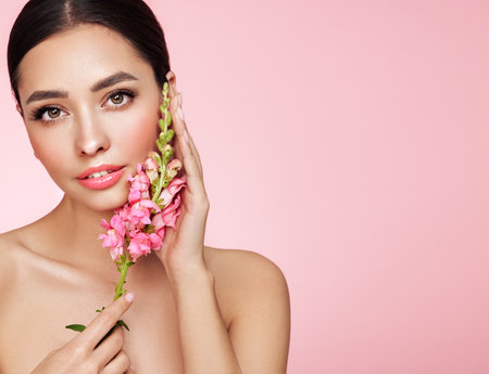 Portrait beautiful young woman with clean fresh skin. Model with healthy skin, close up portrait. Cosmetology, beauty and spa. Girl with a pink  flowerの写真素材