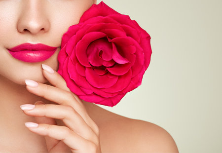Beautiful model with a rose. Perfect woman face makeup close up. Lipstick. Beautiful nails. Nice smile. Perfect skinの写真素材