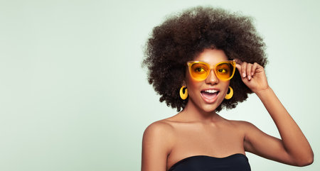 Beauty portrait of African American girl in colored sunglasses. Beautiful black woman. Cosmetics, makeup and fashionの写真素材