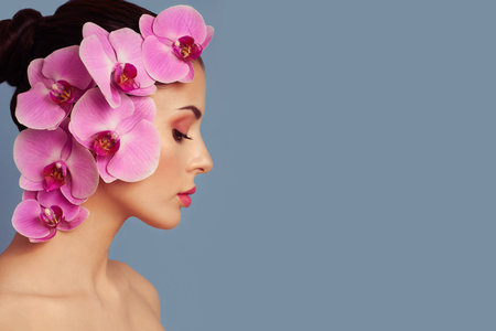 Portrait of beautiful young woman with orchid. Brunette woman with luxury makeup. Perfect skin. Eyelashes. Cosmetic eyeshadow. Purple flowersの写真素材