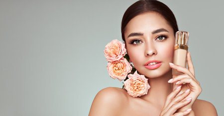 Portrait beautiful young woman with clean fresh skin. Model with foundation makeup bottle. Beautiful young woman with a rose flowerの写真素材