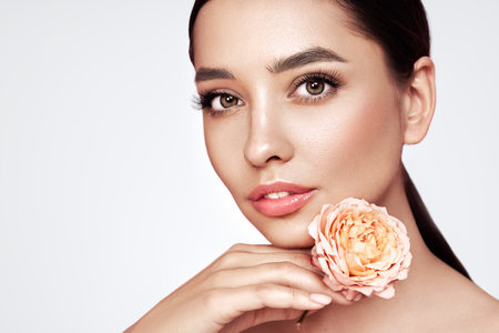 A beautiful young woman with shiny wavy brunette hair. Girl with a pink flower. Model with healthy skin. Cosmetology, beauty and spaの写真素材