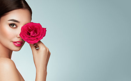 Beautiful model with a rose. Perfect woman face makeup close up. Lipstick. Beautiful nails. Nice smile. Perfect skinの写真素材