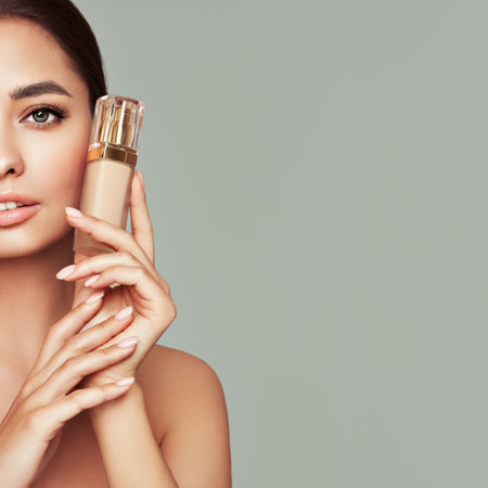 Portrait beautiful young woman with clean fresh skin. Model with foundation makeup bottle. Cosmetology, beauty and spaの写真素材