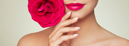 Beautiful model with a rose. Perfect woman face makeup close up. Lipstick. Beautiful nails. Nice smile. Perfect skinの写真素材