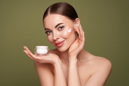 Beauty woman applying cream on her face. Young woman with clean fresh skin. Model with a jar of face creamの写真素材