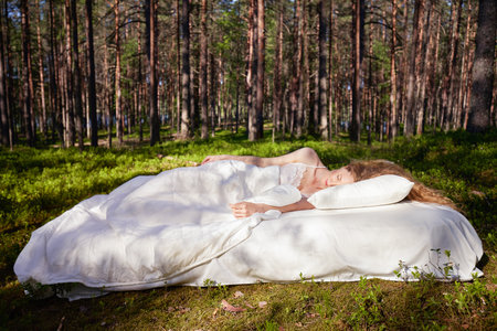 Woman sleeps on a mattress in the summer forest. The girl is resting in natureの写真素材