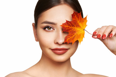 Portrait of beautiful young woman with autumn leafs. Healthy clean fresh skin natural make up beauty eyes and red nailsの写真素材