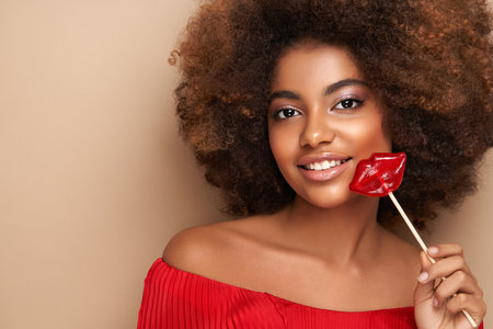 Beautiful portrait of an African girl with a lips shaped lollipop. Valentine's Day. Symbol of loveの写真素材