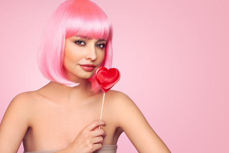 Beauty model portrait with pink hair. Bob short Haircut. Beautiful glamorous girl with a heart-shaped lollipopの写真素材