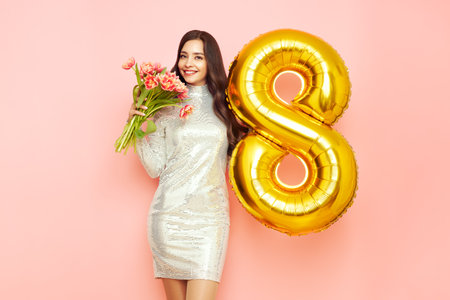 Beautiful young woman hold bouquet of tulips flowers and balloon number 8, rejoices spring holiday. Women's Day on March 8thの写真素材