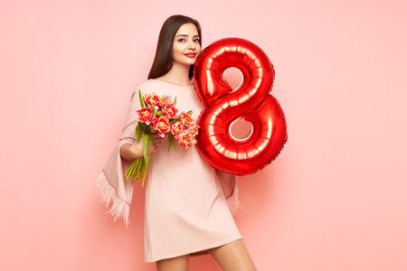 Beautiful young woman hold bouquet of tulips flowers and balloon number 8, rejoices spring holiday. Women's Day on March 8thの写真素材