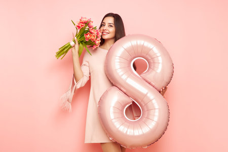 Beautiful young woman hold bouquet of tulips flowers and balloon number 8, rejoices spring holiday....