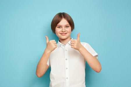 Smiling cheerful child showing thumbs up, highlighted on a blue backgroundの写真素材