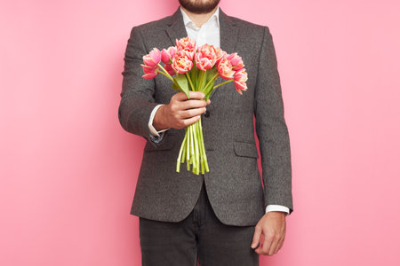Romantic man in suit, with bouquet of tulips on isolated pink background, Valentine's Day, March 8の写真素材