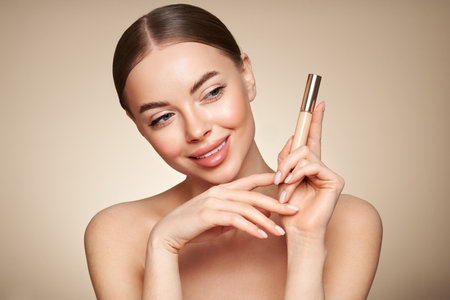 Portrait beautiful young woman with clean fresh skin. Model with foundation makeup bottle. Cosmetology, beauty and spaの写真素材