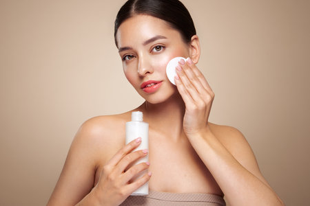 Young girl holds cotton pad while cleansing face with cosmetic milk. Skin care removal of makeup cleansing. Basic facial skin careの写真素材