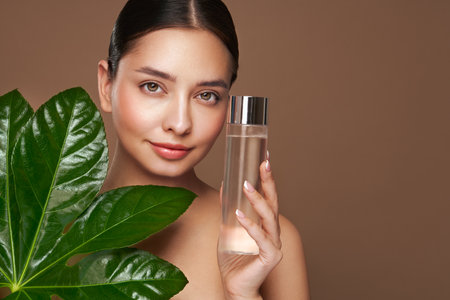 Close up woman face with green exotic leaf. Skin care beauty treatments concept. Model with clean health skin of face. Woman holds bottle with cosmetic tonicの写真素材