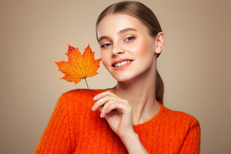 Portrait of beautiful young woman in orange blouse with autumn leafs. Healthy clean fresh skin natural make up beauty eyesの写真素材