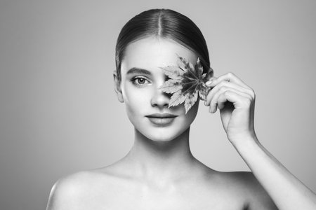 Portrait of beautiful young woman with autumn leafs. Healthy clean fresh skin natural make up beauty eyes. Black and white photoの写真素材
