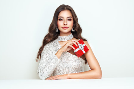 Beautiful woman in cocktail dress with gift box in hands. Beauty model with long curly hair. Christmas or New Year festivities. Holiday and Partyの写真素材