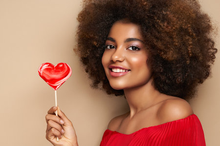 Beautiful portrait of an African girl with a heart shaped lollipop. Valentine's Day. Symbol of loveの写真素材