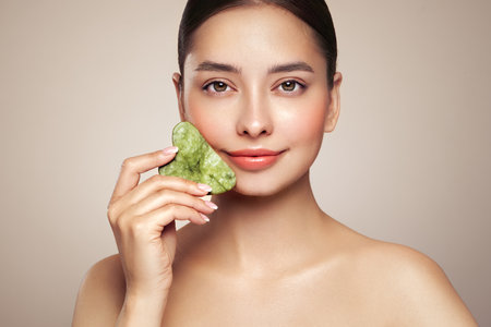 Beauty young woman doing skin care routine, scrapping, massage facial skin with jade gua sha scrapper, Facial treatment for anti aging and cosmetic cleaningの写真素材