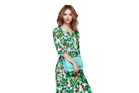 Blonde young woman in floral spring summer dress. Girl posing on a transparent background. Summer floral outfit. Fashion photo. Glamour lady with handbagの写真素材