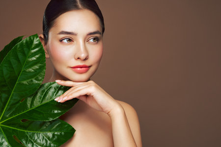 Close up woman face with green exotic leaf. Skin care beauty treatments concept. Model with clean, health skin of faceの写真素材
