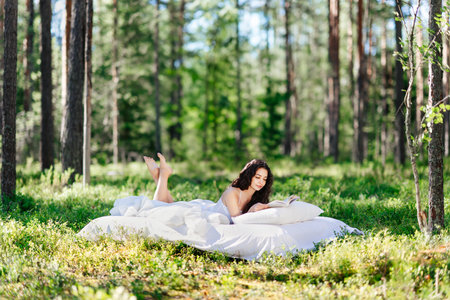 Young woman is reading a book in the forest lying on a mattress. The girl relaxing in natureの写真素材