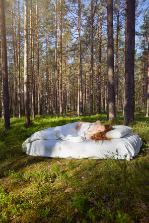 Woman sleeps on a mattress in the summer forest. The girl is resting in natureの写真素材