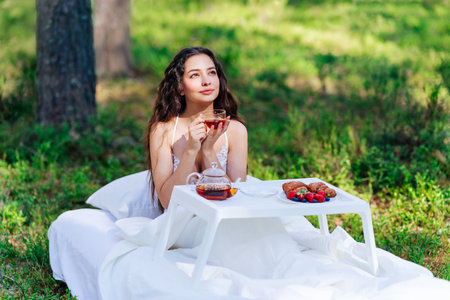 Woman wakes up in a summer forest. Young woman has breakfast in bed in a summer forestの写真素材