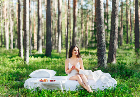 Woman wakes up in a summer forest. Young woman has breakfast in bed in a summer forestの写真素材